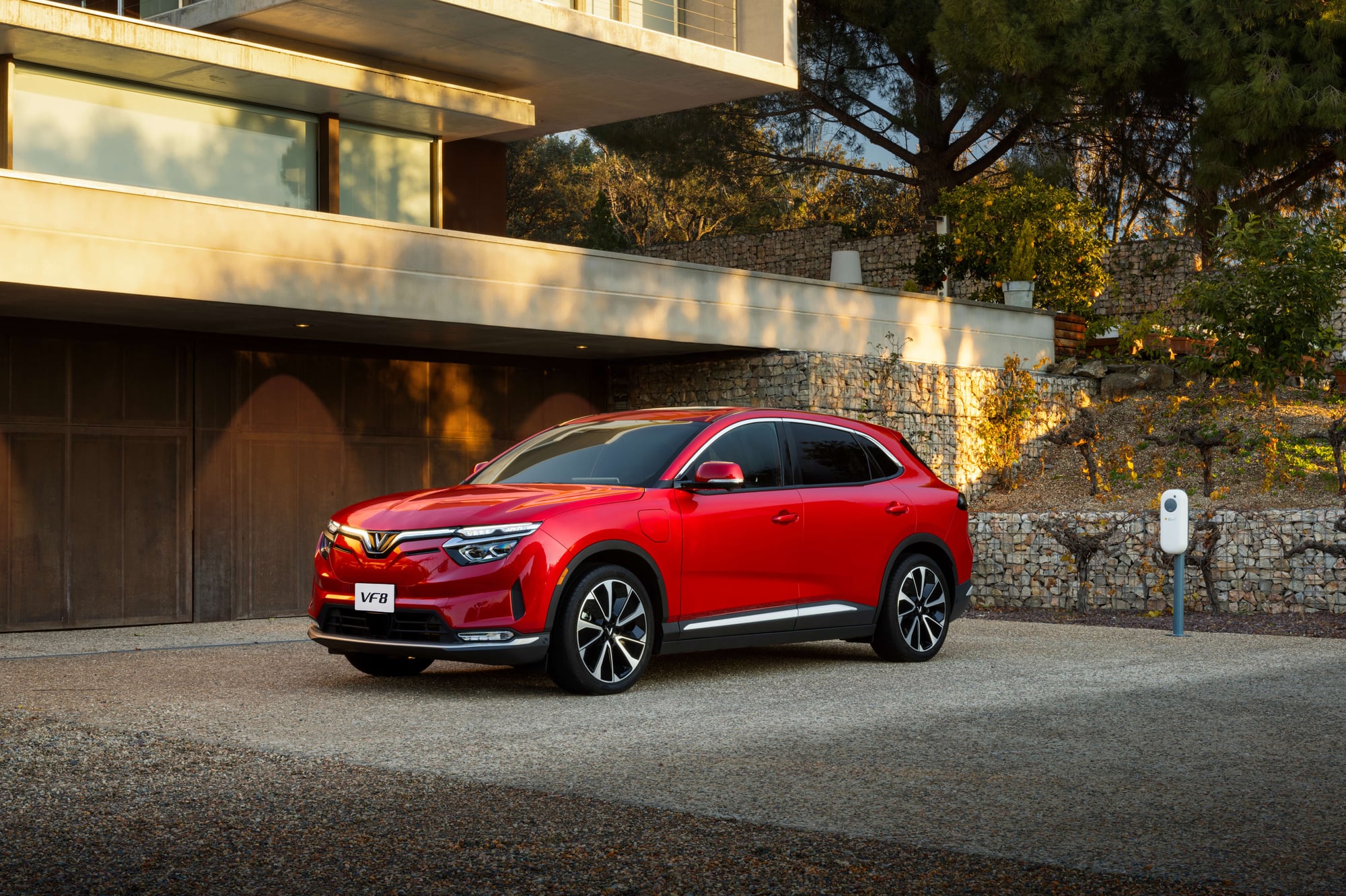 VinFast VF 8 in red at dusk beside a home charger, front three-quarter view