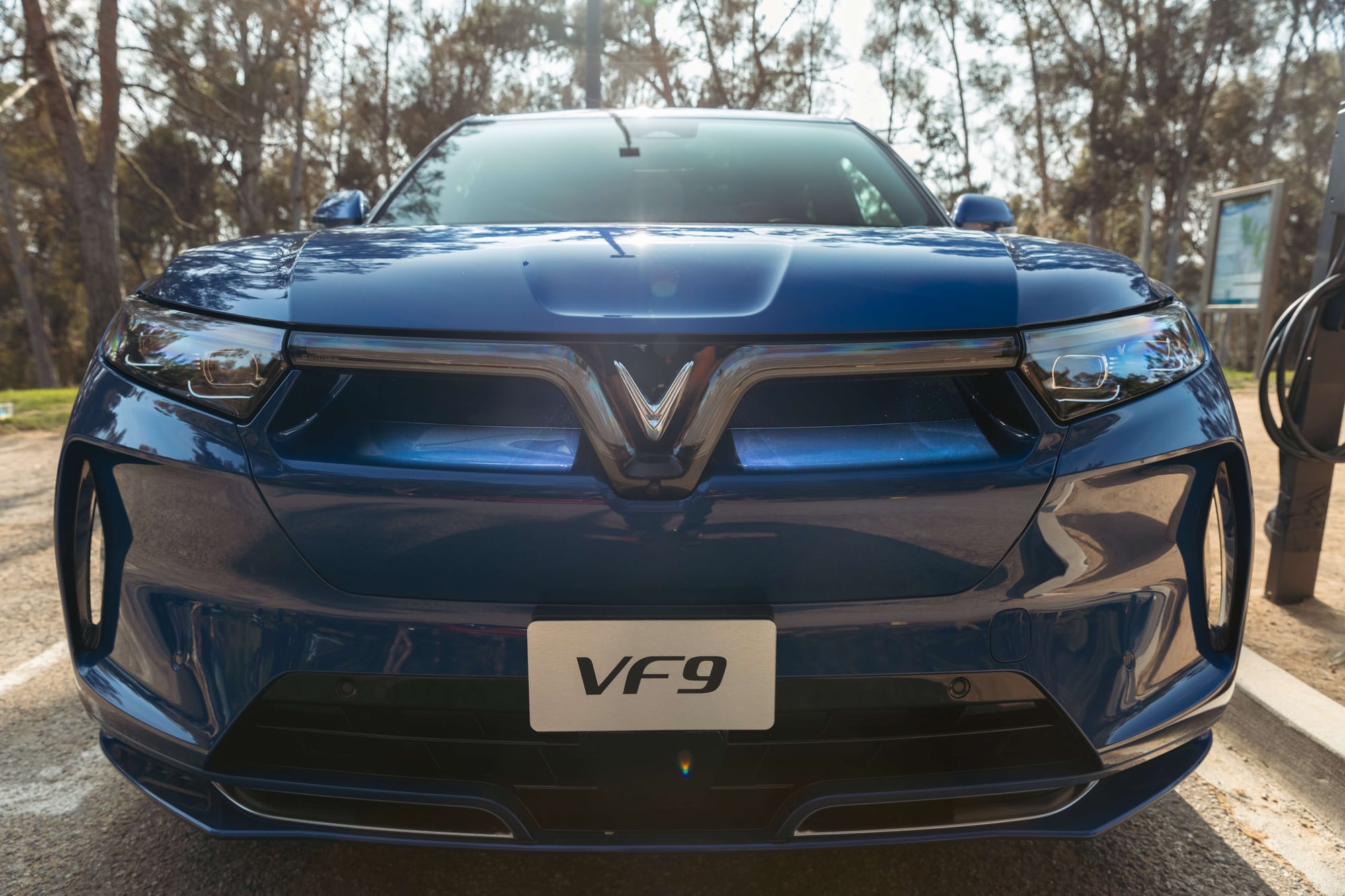 VinFast VF 9 in blue, head-on, parked at a charging station among trees